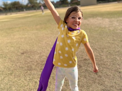 Girls on the Run participant smiles outdoors with arms outstretched in super hero pose